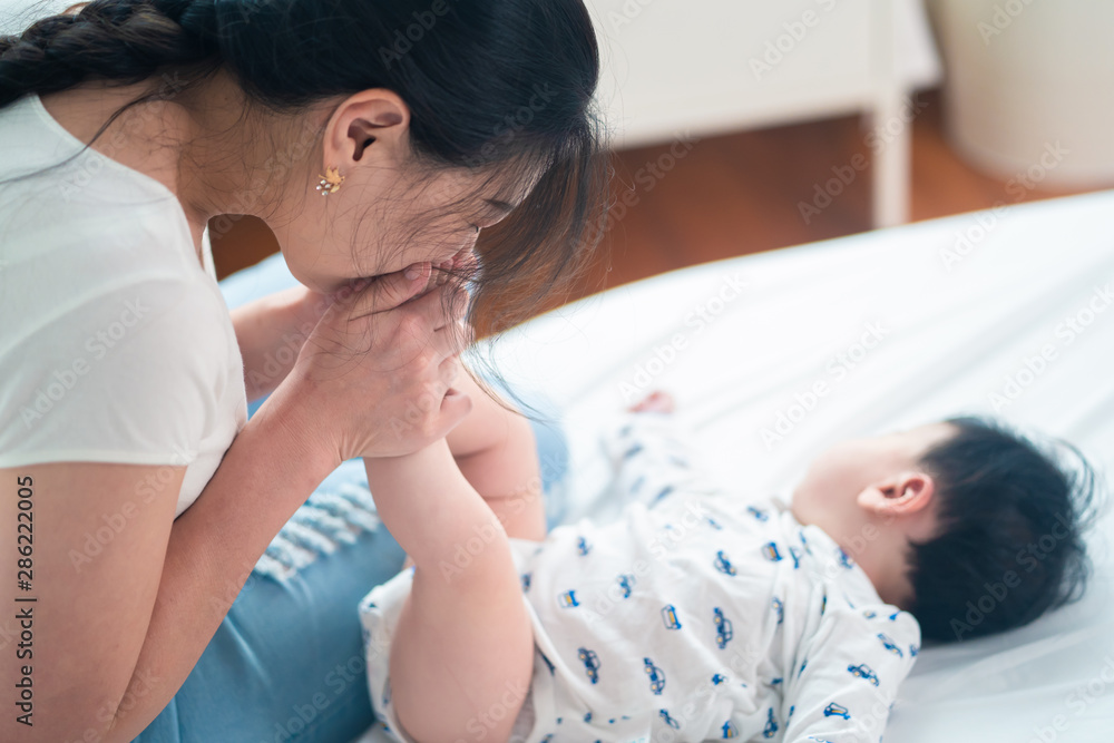 亚洲妈妈在床上亲吻她可爱的新生婴儿的脚。她微笑着抱着可爱的k