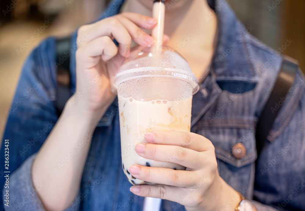 Young girl in denim jacket is drinking brown sugar flavored tapioca pearl bubble milk tea with glass