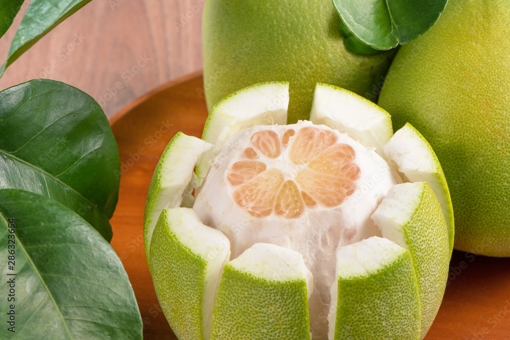 Fresh peeled pomelo, grapefruit, shaddock with green leaves on dark wooden plank table. Seasonal fru