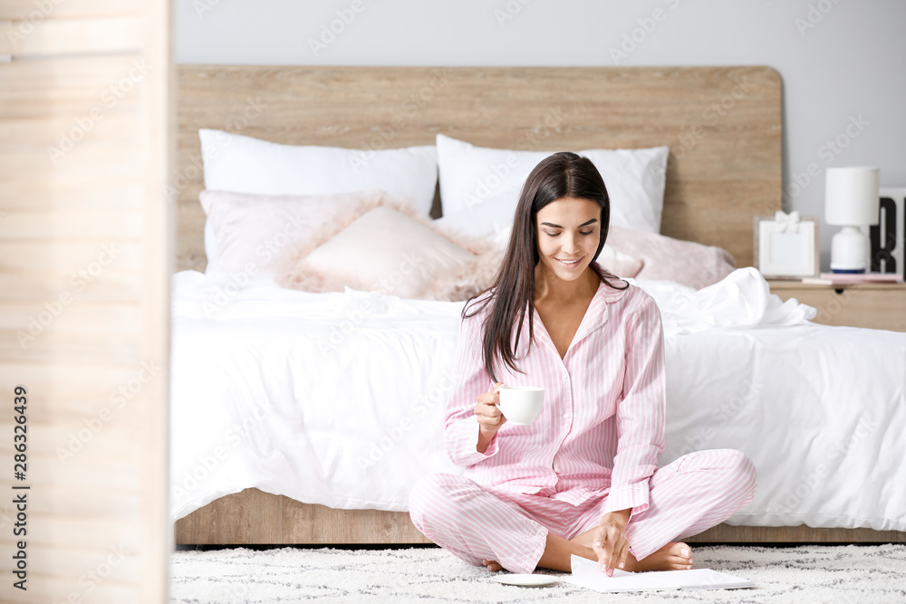 Morning of beautiful young woman drinking coffee while reading book in bedroom