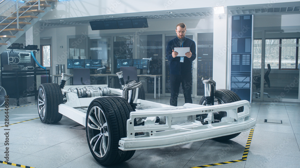 Engineer with Glasses and Beard Scans Electric Car Chassis Prototype with Wheels, Batteries and Engi