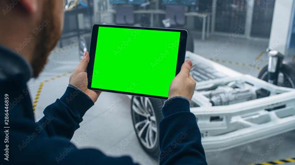 Engineer with Glasses and Beard Scans Electric Car Chassis Prototype with Wheels, Batteries and Engi