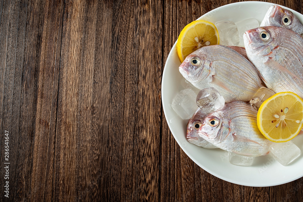 A plate of fresh red mullet and spices ingredients on a wooden board background