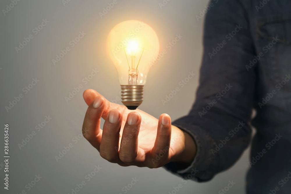 concept idea and inspiration saving power energy. man hand holding light bulb in room