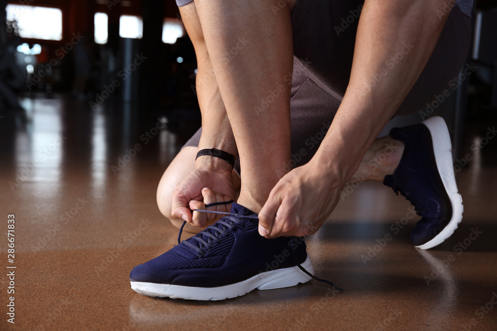 Sporty young man tying shoelaces in gym