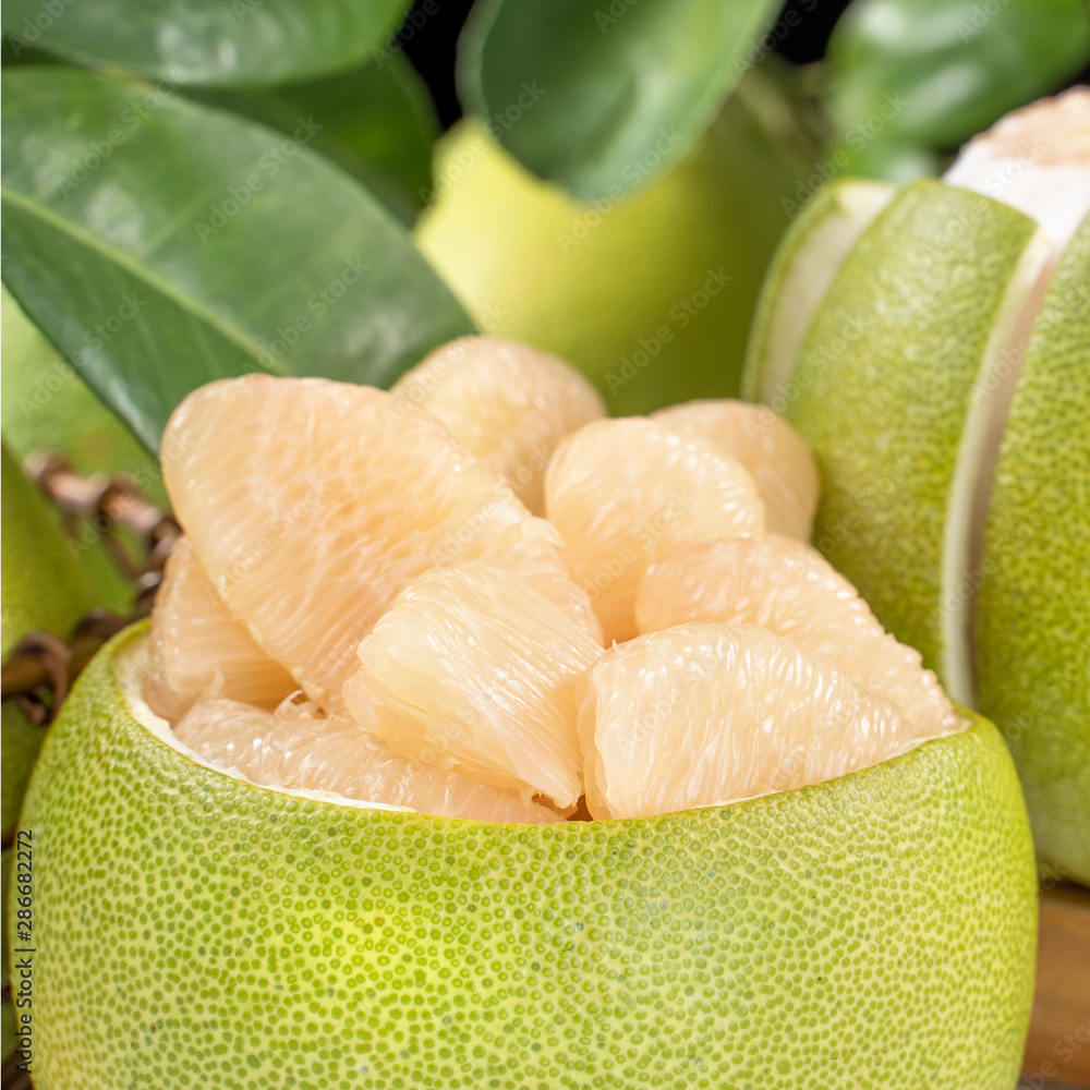 Fresh peeled pomelo, grapefruit, shaddock with green leaf on bright wooden plank table. Seasonal fru