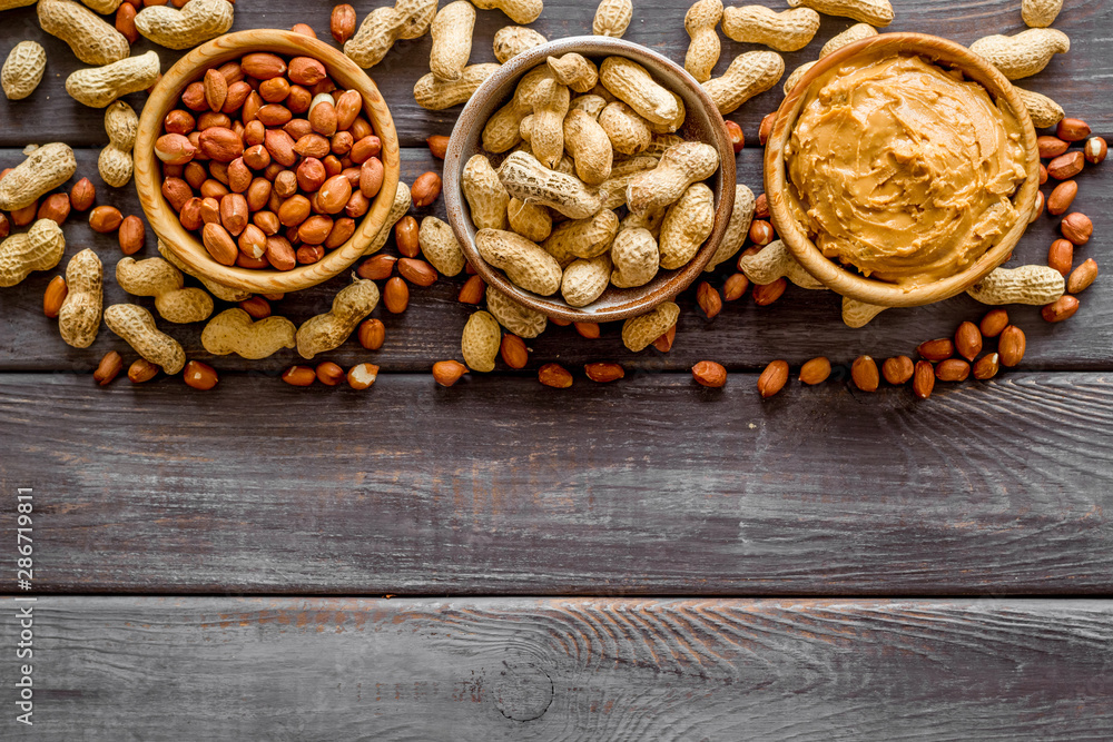 Product for hearty breakfast with peanut butter in bowl near nuts on wooden background top view mock