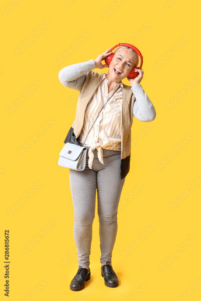 Stylish mature woman listening to music on color background