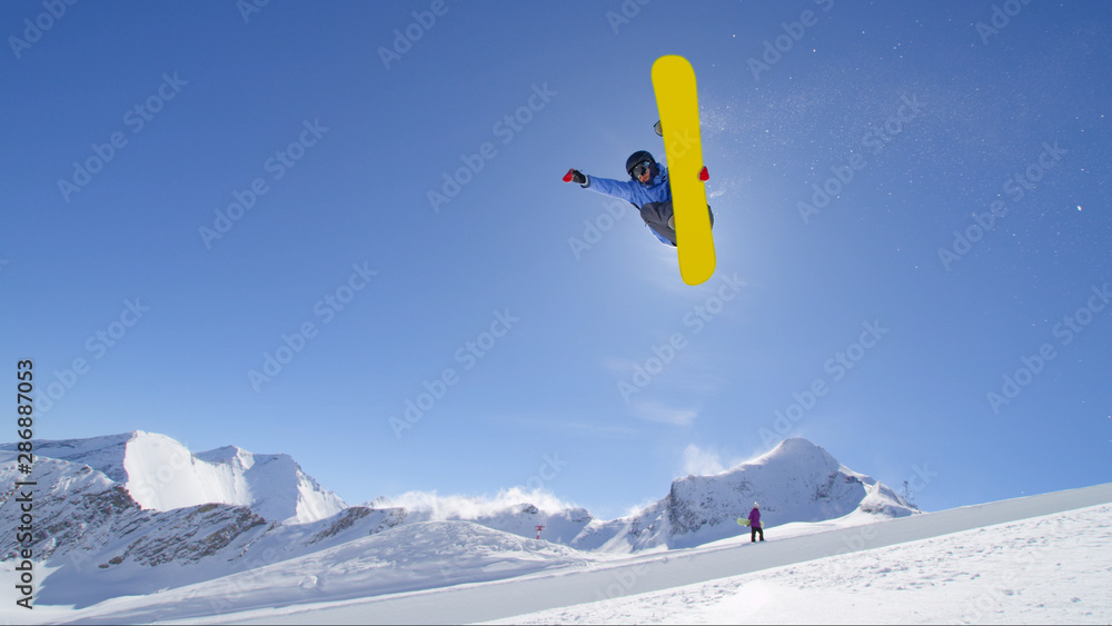 Young pro snowboarder jumping in half pipe in sunny snow park