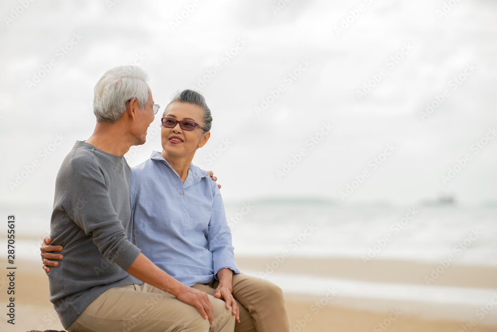 Happy asian senior couple  have fun and enjoy at the beach, senior man and woman hugging while sitti