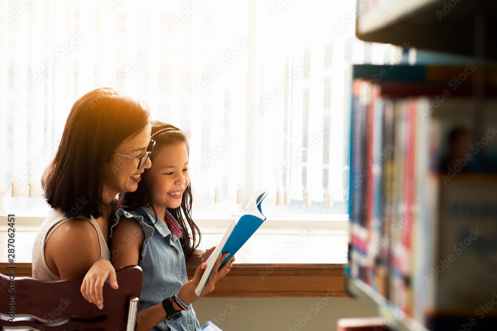 Happy Asia woman  in eyeglasses reading a book with her daughter at a bookstoreor library , Relaxing