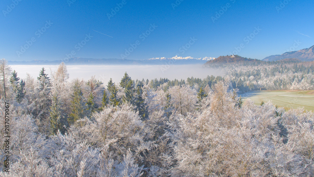 空中飞航：冬天高高的雪山和结冰的森林后面的小教堂