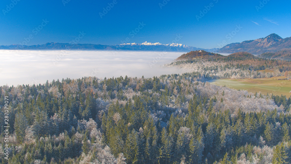 航空：雾蒙蒙的冬天，高高的雪山和结冰的森林后面的教堂