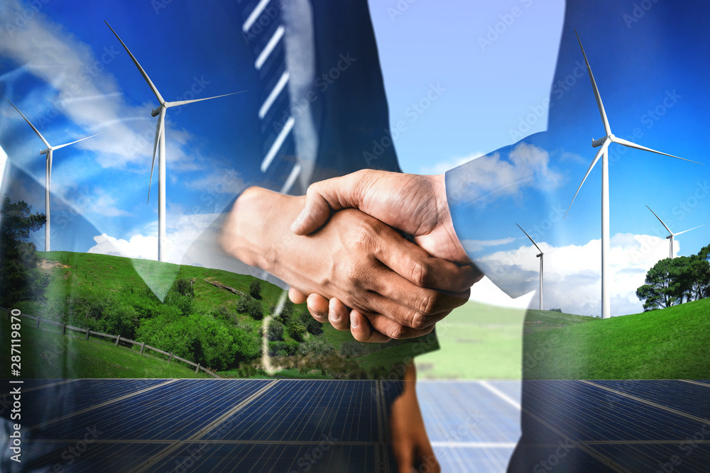 Double exposure graphic of business people handshake over wind turbine farm and green renewable ener