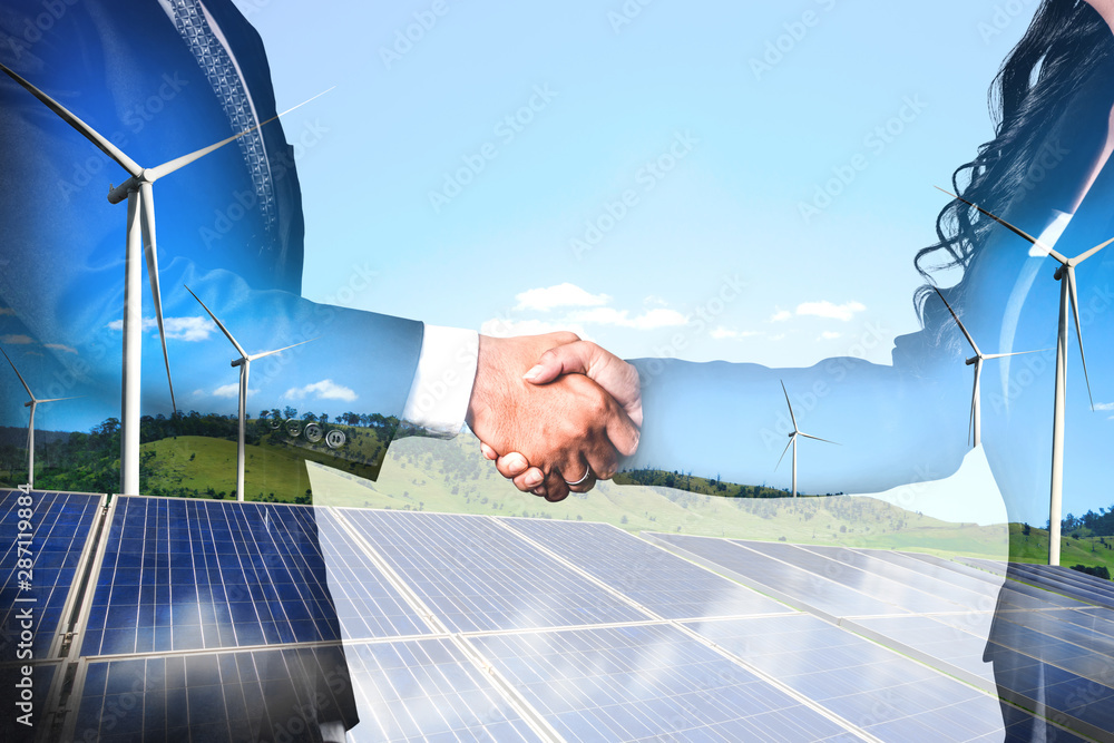 Double exposure graphic of business people handshake over wind turbine farm and green renewable ener