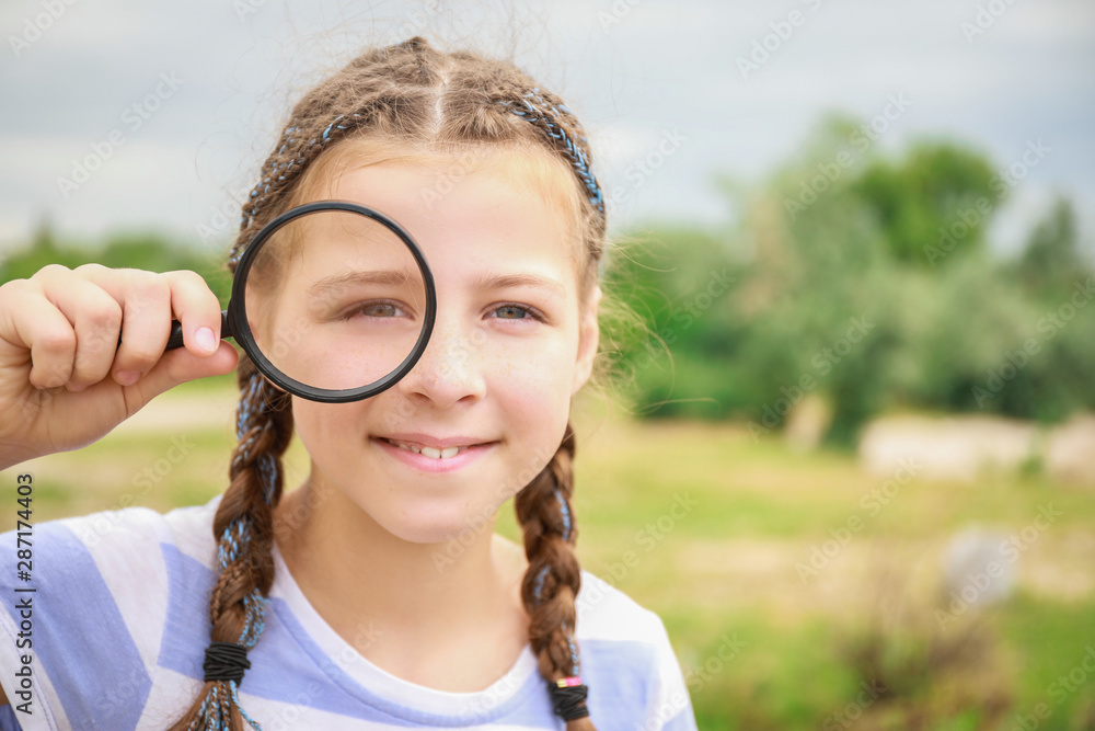 Little girl with magnifying glass studying nature outdoors