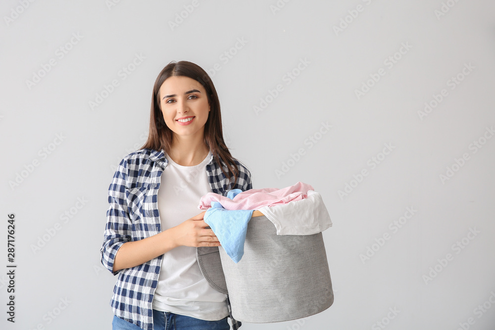 Beautiful young woman with laundry on light background