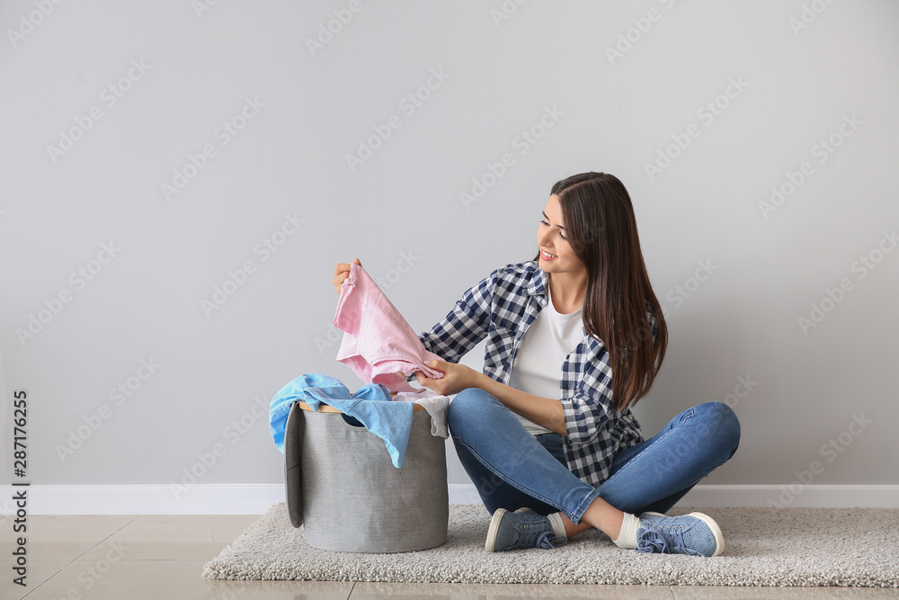 漂亮的年轻女子坐在白墙附近的地板上洗衣服