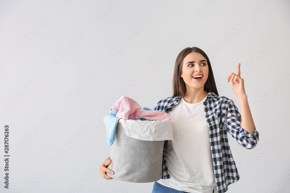 Beautiful young woman with laundry and raised index finger on light background