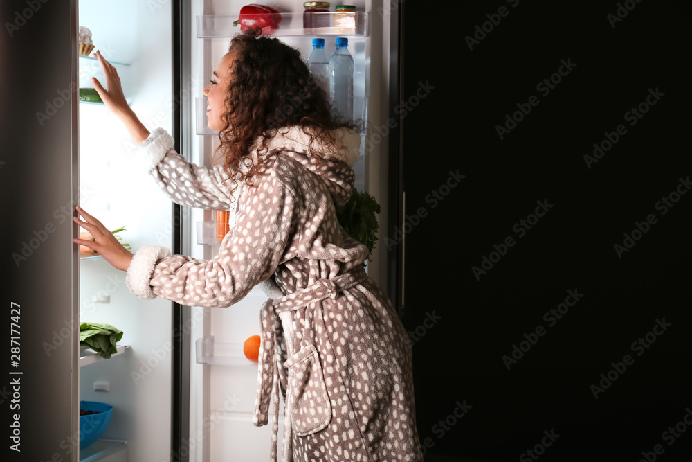 年轻女子晚上在冰箱里挑选食物