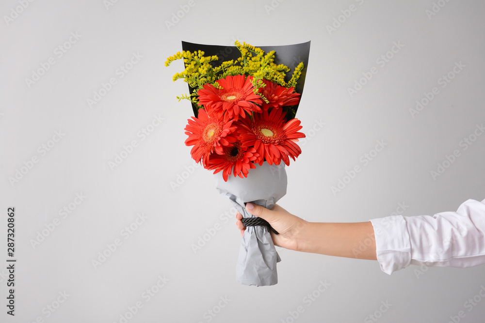 Woman with bouquet of beautiful gerbera flowers on light background