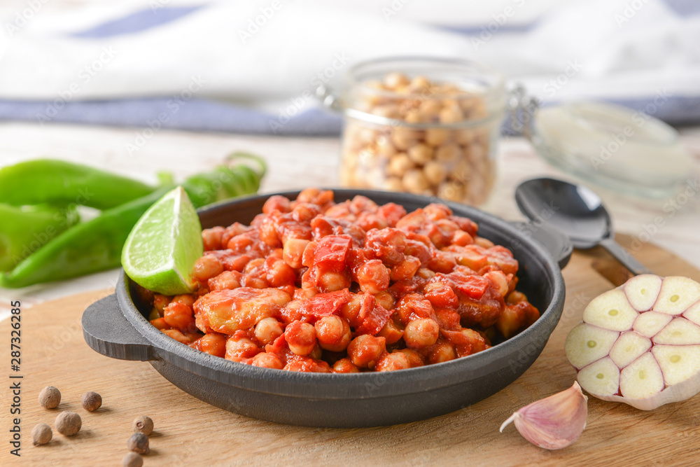 Frying pan with tasty chickpea in tomato sauce on table