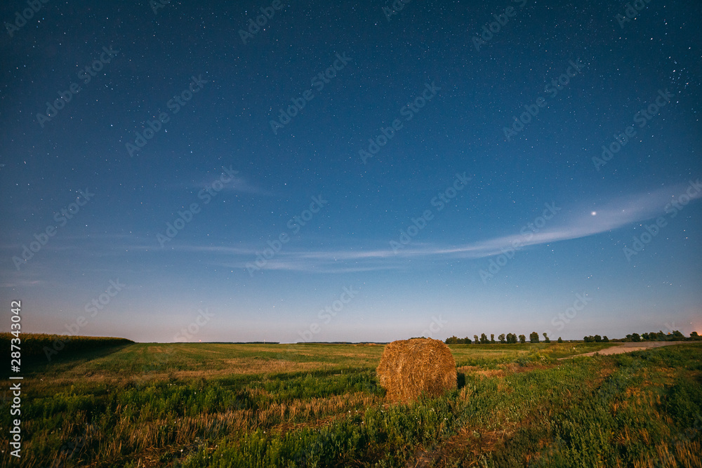 Natural Night Starry Sky Above Field Meadow With Hay Bale After Harvest. Glowing Stars Above Rural L