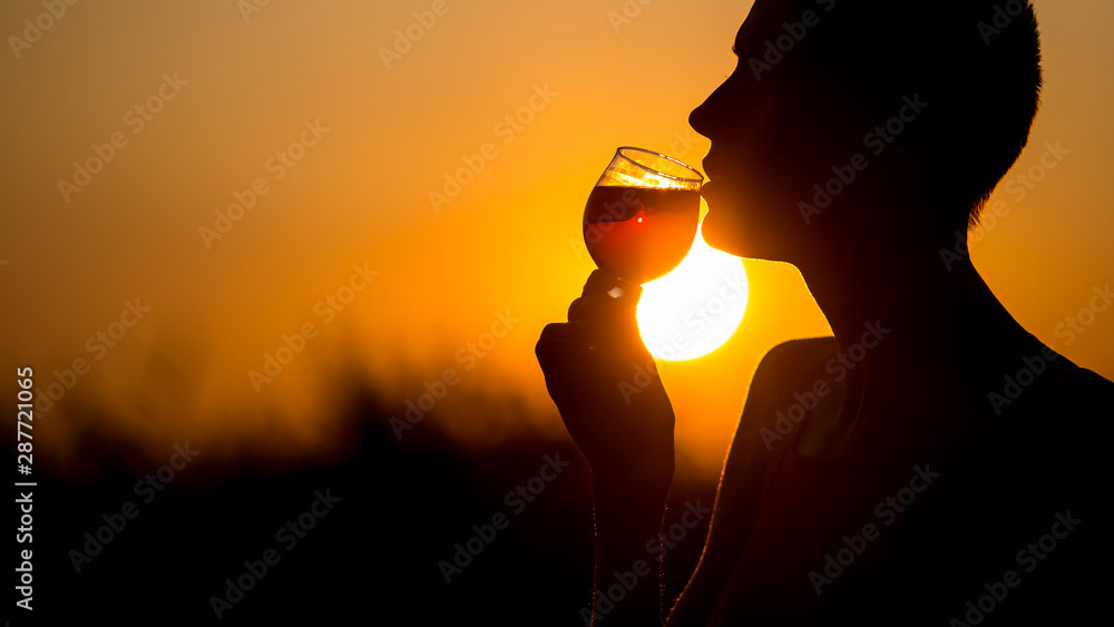 Woman with a cocktail over suset sky in orange colors.