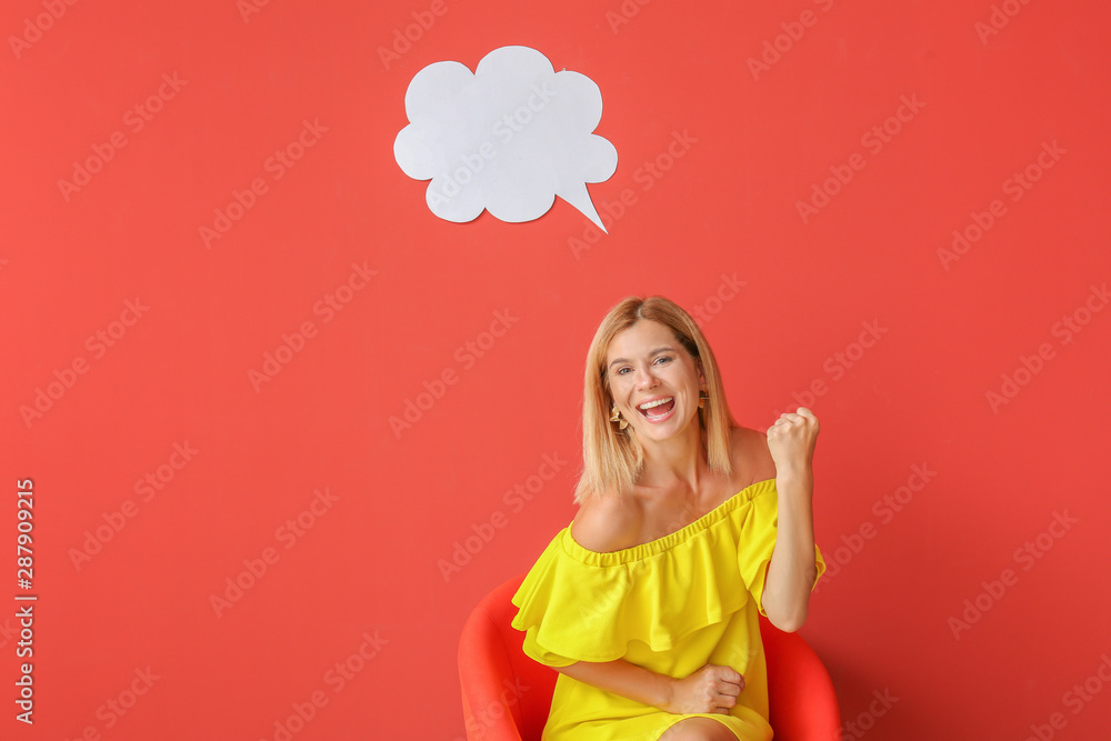 Happy woman sitting in armchair near speech bubble on color background