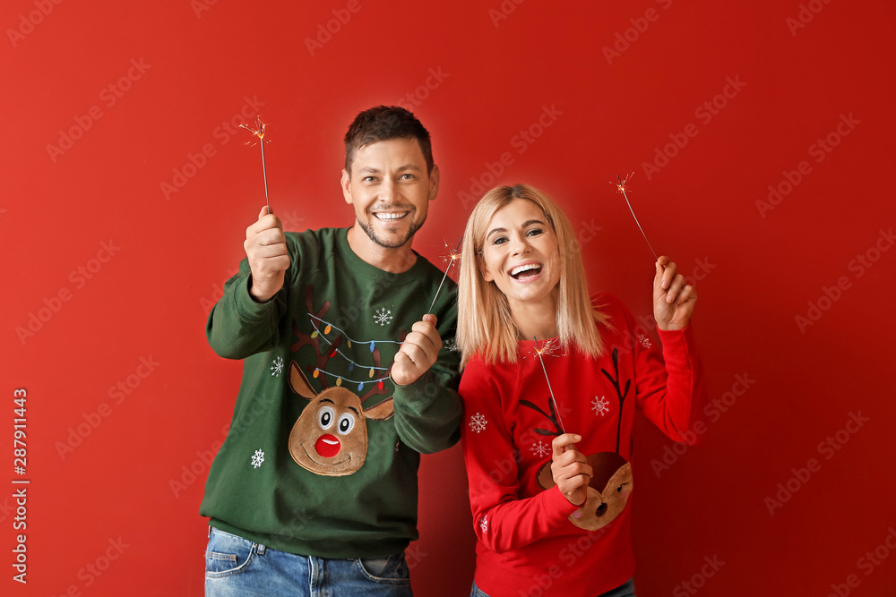 Happy couple with Christmas sparklers on color background