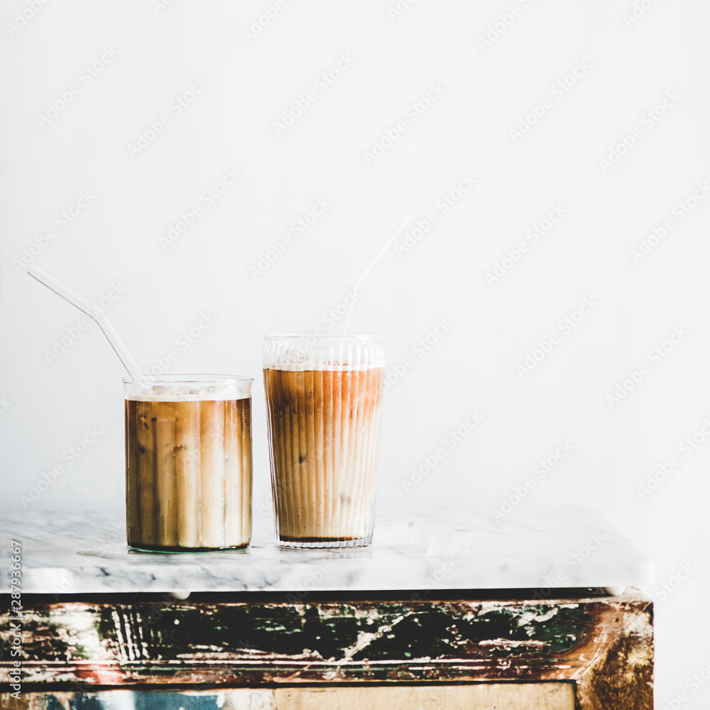 Homemade iced latte coffee in glasses with straws on grey marble table, white wall at background, co