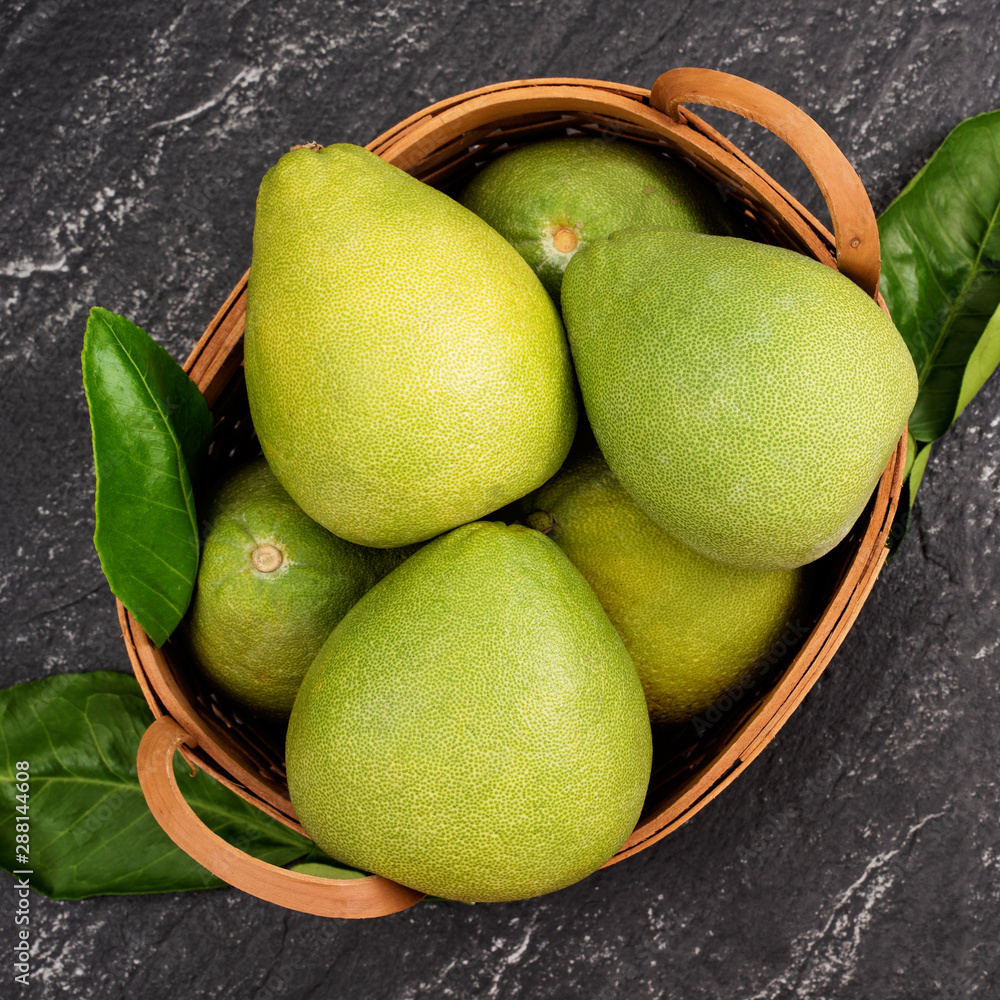 Fresh pomelo,grapefruit in bamboo basket with green leaf on dark black slate background. Seasonal fr