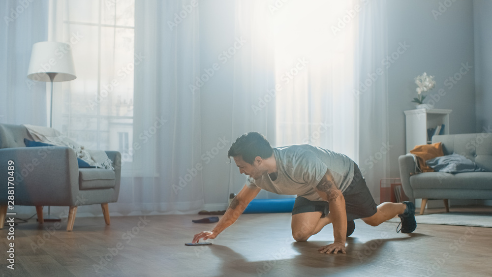 Athletic Fit Man in T-shirt and Shorts is Doing Mountain Climber Exercises While Using a Stopwatch o