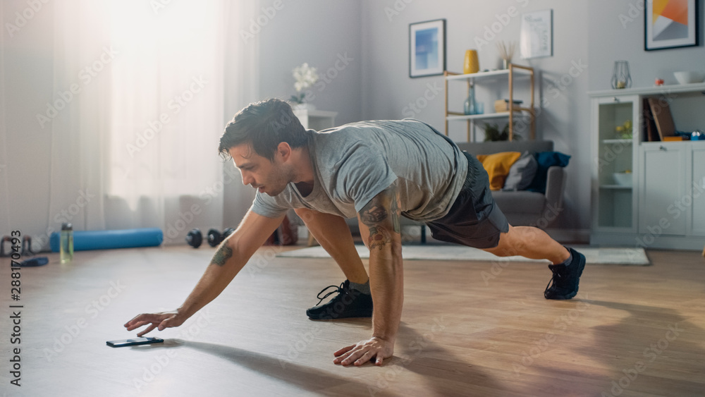 Muscular Athletic Fit Man in T-shirt and Shorts is Doing Mountain Climber Exercises While Using a St