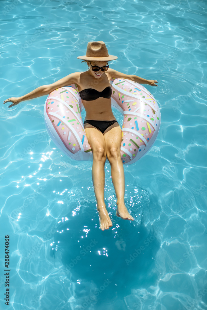 Woman in swimsuit and hat swimming with inflatable ring in the form of a donut in the water pool, vi