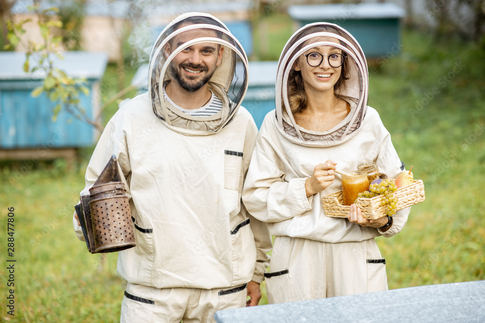 Portrait of a man and woman beekepers in protective uniform standing together with beesmoker and hon