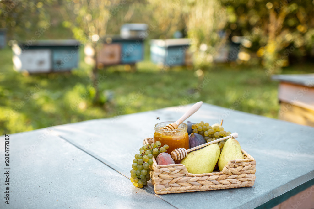 Composition of sweet fruits and jar with honey on the beehive at the apiary, image with copy space