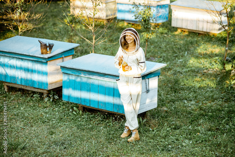 Full body portrait of a female beekeeper in protective uniform on the apiary outdoors