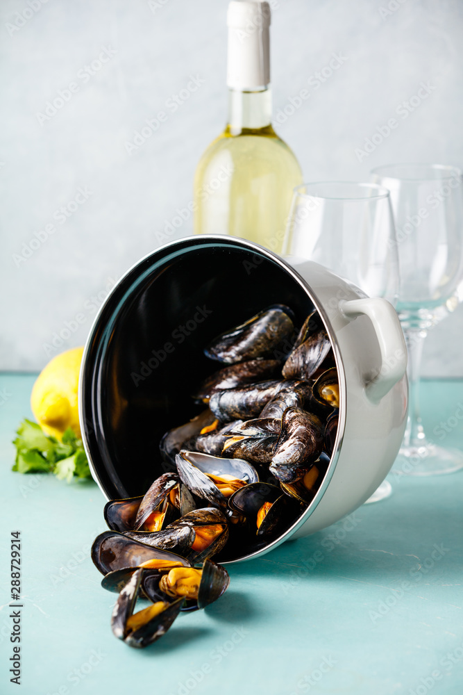 Pot of steamed mussels with lemon, herbs and white wine on blue background