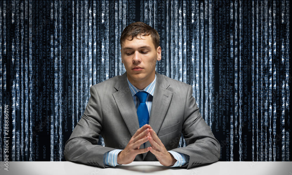 Young serious man folded hands and sitting at desk