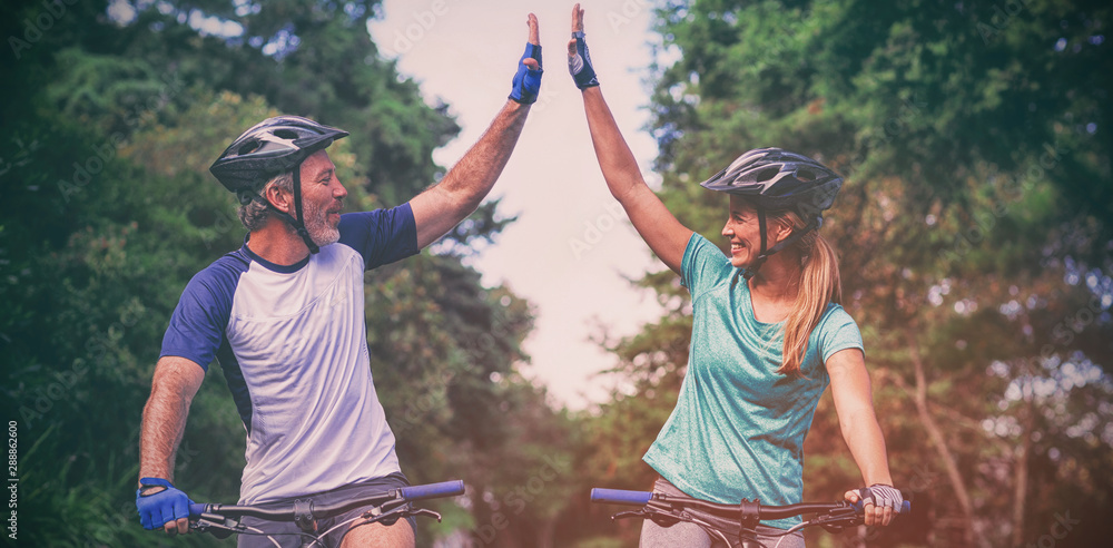 Athletic couple giving high five while riding bicycle on the road