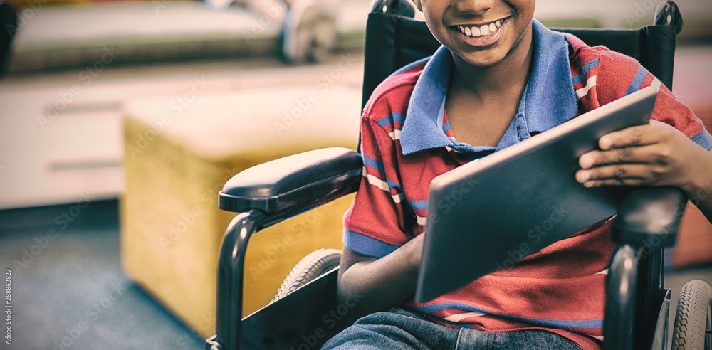 Disabled schoolboy on wheelchair using digital tablet in library