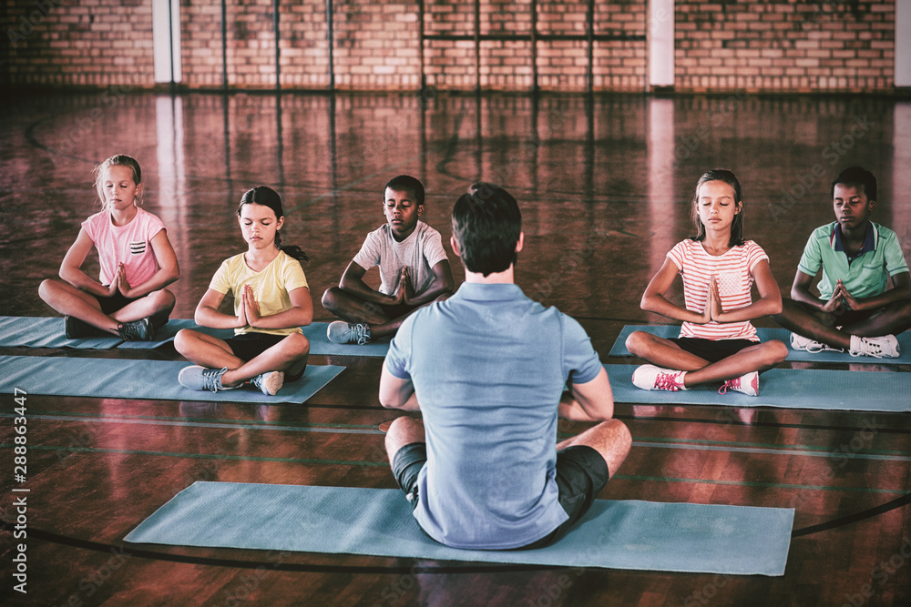 School kids and teacher meditating during yoga class