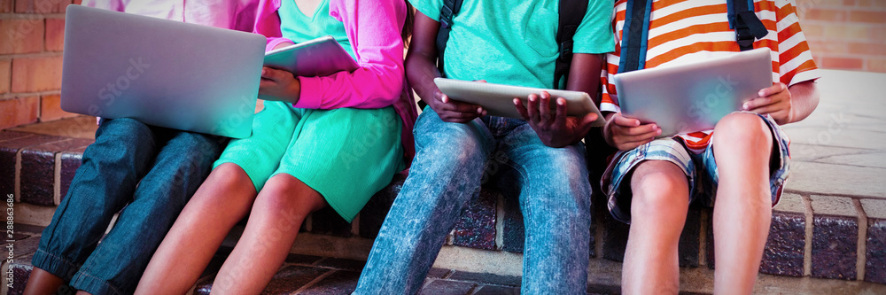 Kids sitting on staircase using laptop and digital tablet 