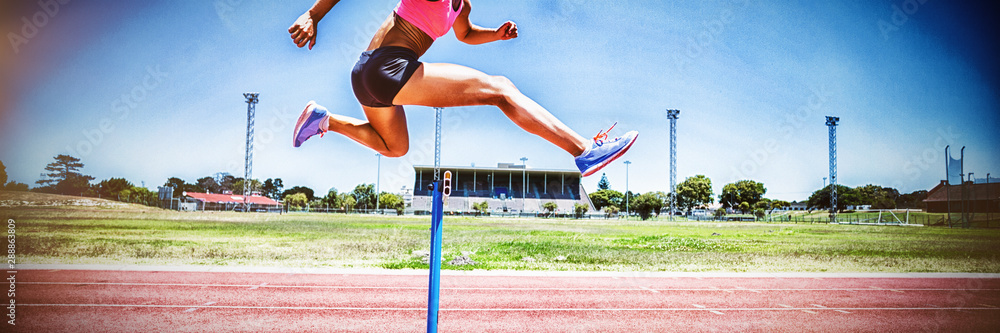 Female athlete jumping above the hurdle