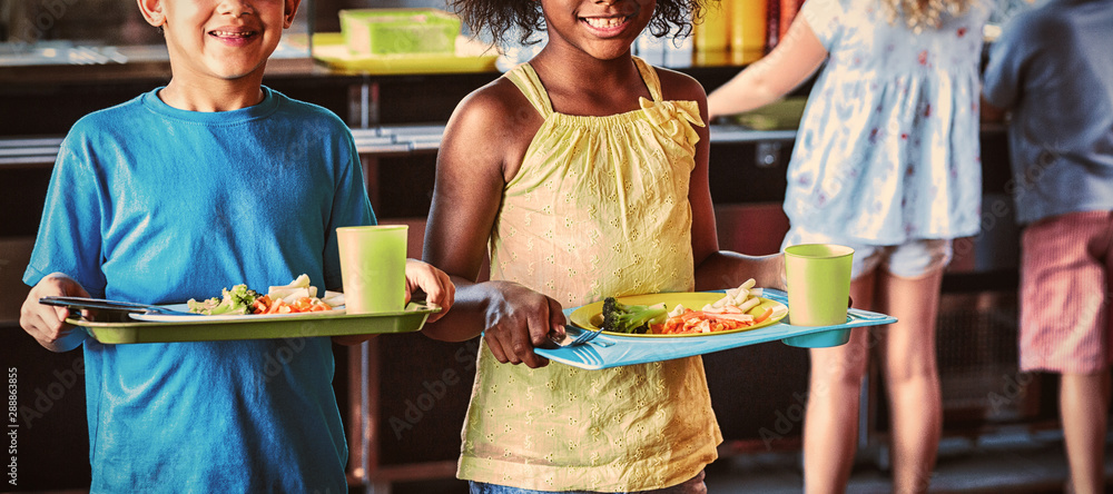 Happy school children holding food tray in canteen