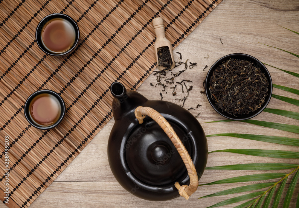 Cup of hot tea with teapot, green tea leaves and dried herbs top view on the wooden table, Organic p