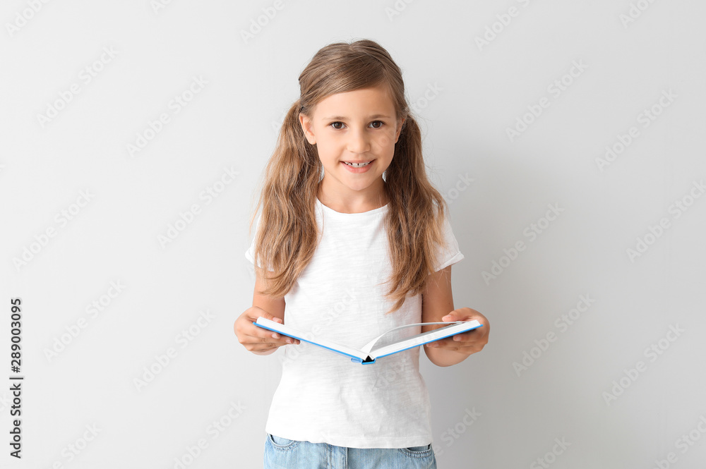 Little girl with book on light background