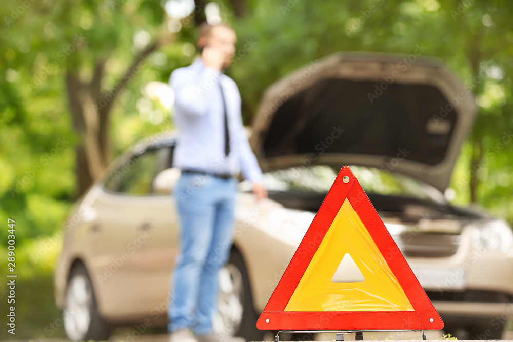 Emergency stop sign and man talking by phone near broken car on road