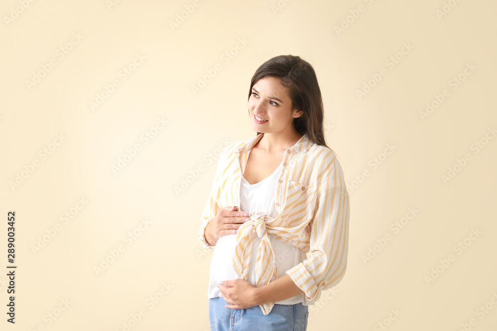 Young pregnant woman on light color background